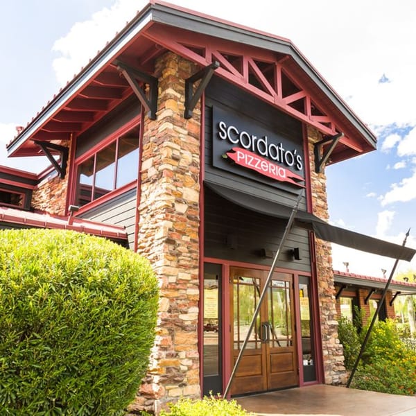 The exterior of Scordato's Pizzeria, featuring a stone and wood facade with a red roof and black awnings.