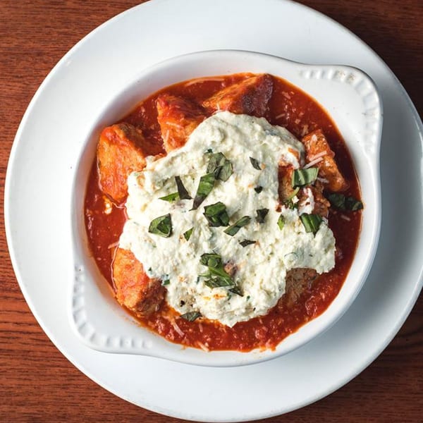 Baked pasta dish with tomato sauce, ricotta cheese, and basil in a white bowl.